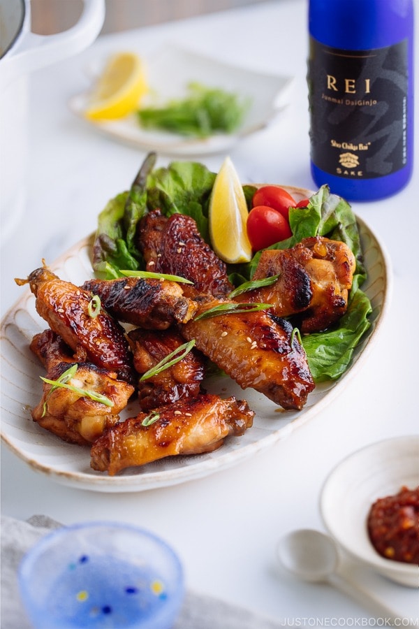 Teriyaki wings served on a white plate garnished with lemon, tomatoes and green lettuce.