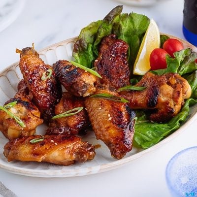 Teriyaki wings served on a white plate garnished with lemon, tomatoes and green lettuce.