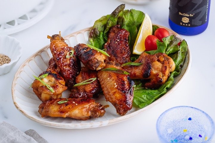 Teriyaki wings served on a white plate garnished with lemon, tomatoes and green lettuce.