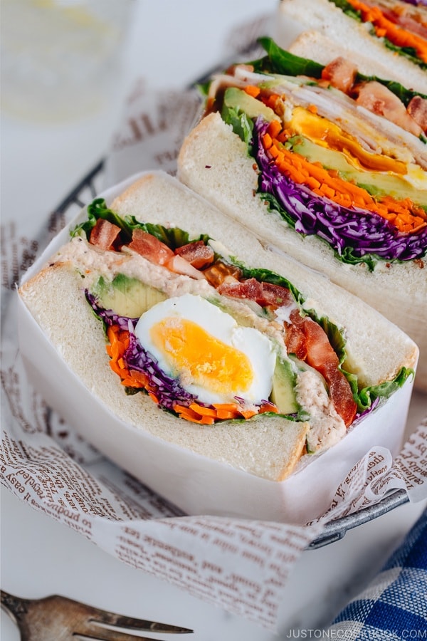 A basket containing 3 kinds of thick colorful Japanese sandwiches called Wanpaku Sandiwch (Sando).