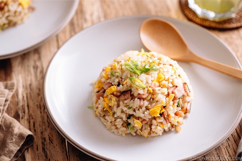 Fried rice with egg, ham, and green onion on a white plate.