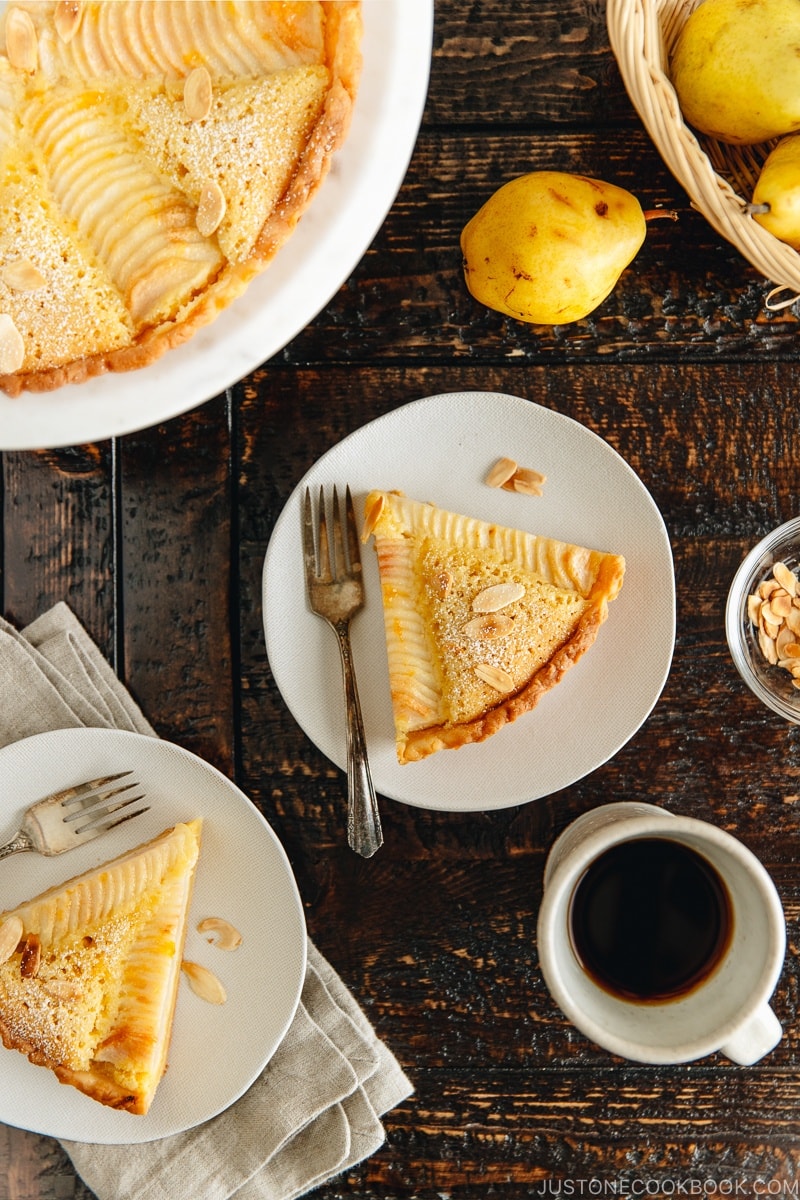 A slice of Pear and Almond Tart (Pear Frangipane Tart) on a plate, served with coffee.