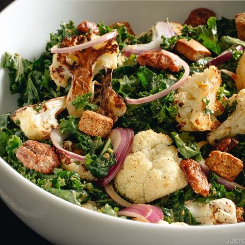 A large white bowl containing Roasted Cauliflower Kale Salad tossed with Miso Tahini Dressing.