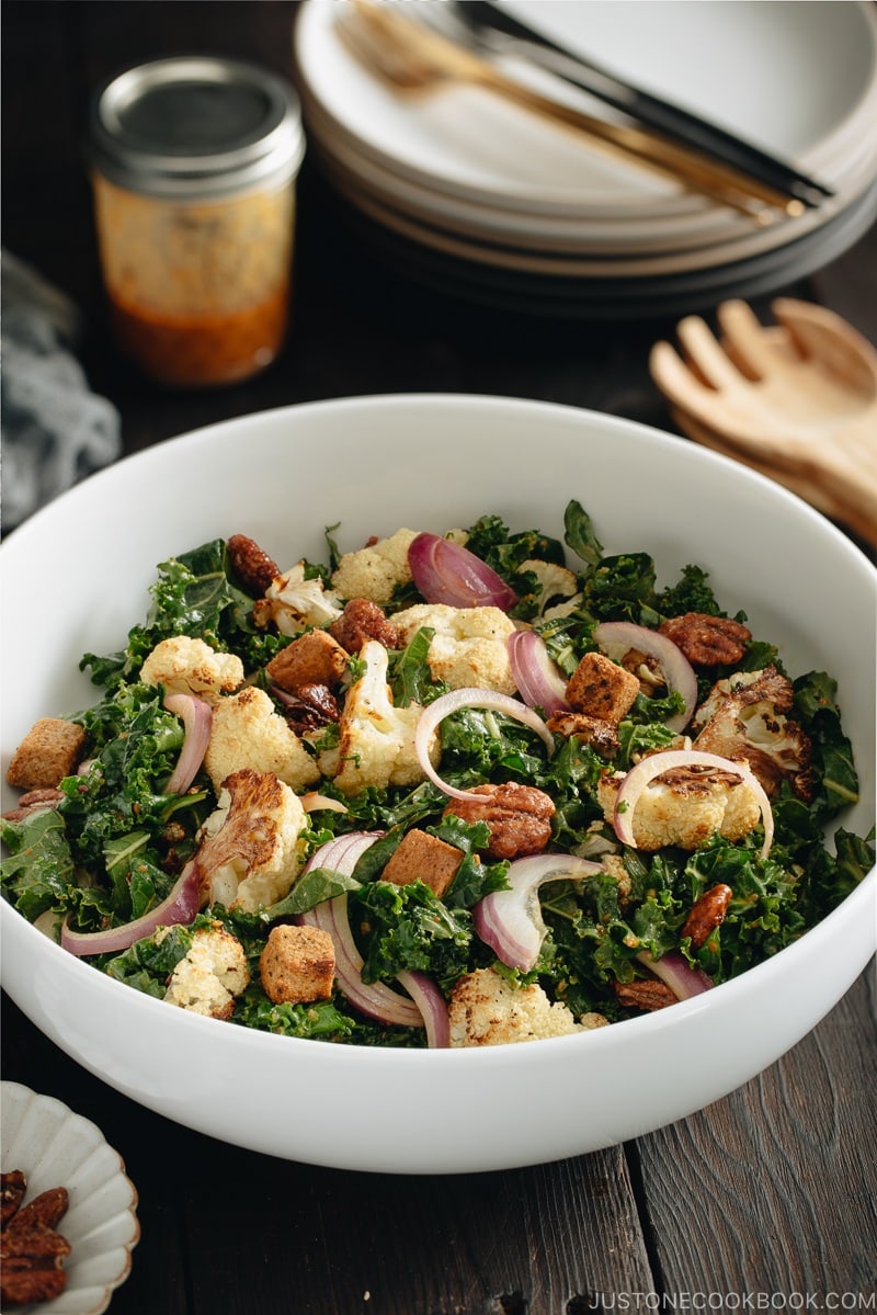 A large white bowl containing Roasted Cauliflower Kale Salad tossed with Miso Tahini Dressing.