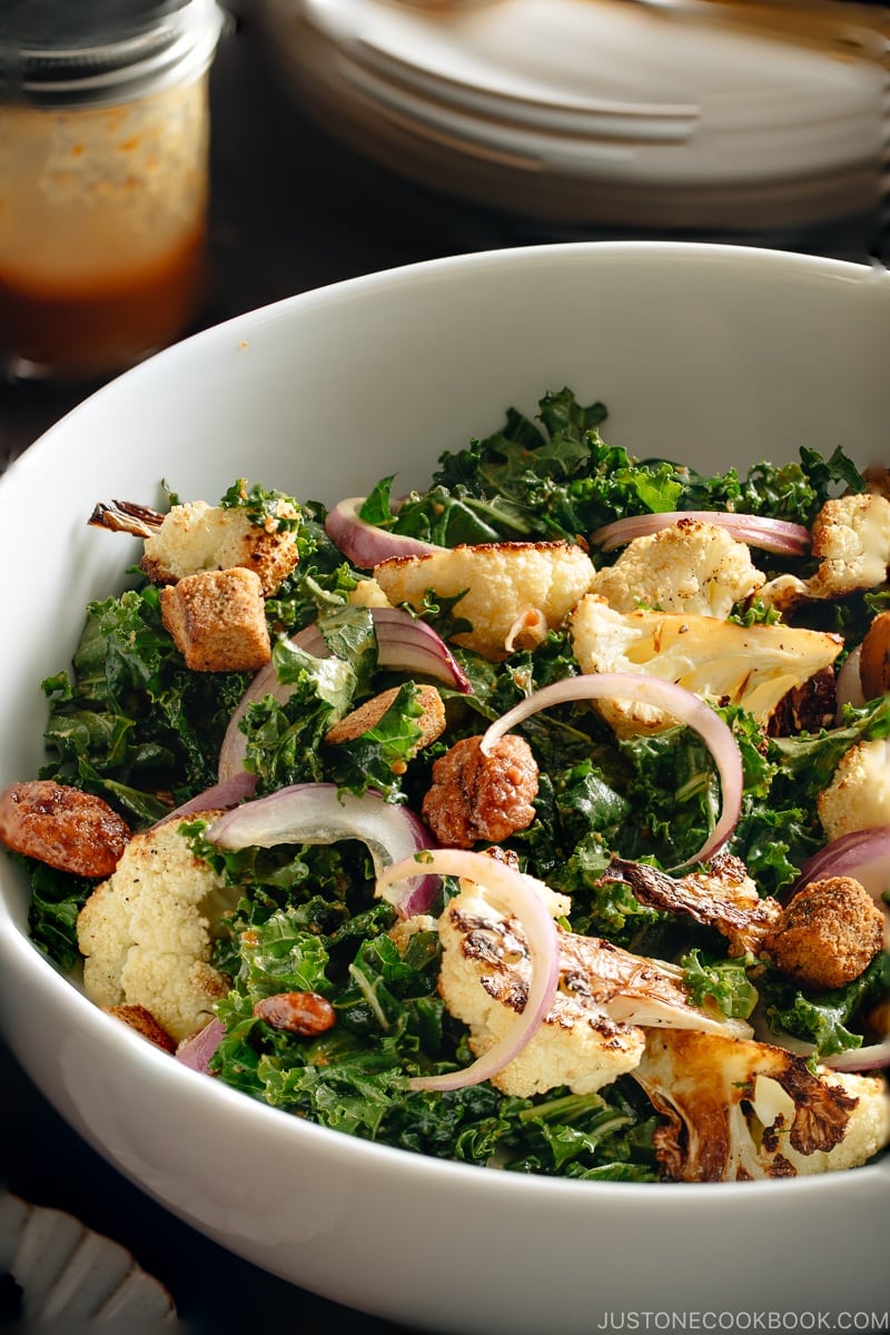 A large white bowl containing Roasted Cauliflower Kale Salad tossed with Miso Tahini Dressing.