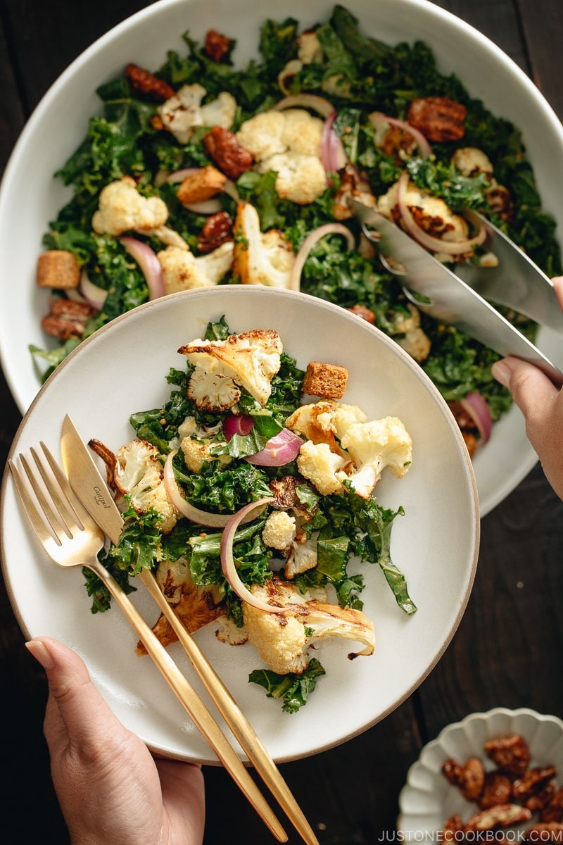 A large white bowl containing Roasted Cauliflower Kale Salad tossed with Miso Tahini Dressing.