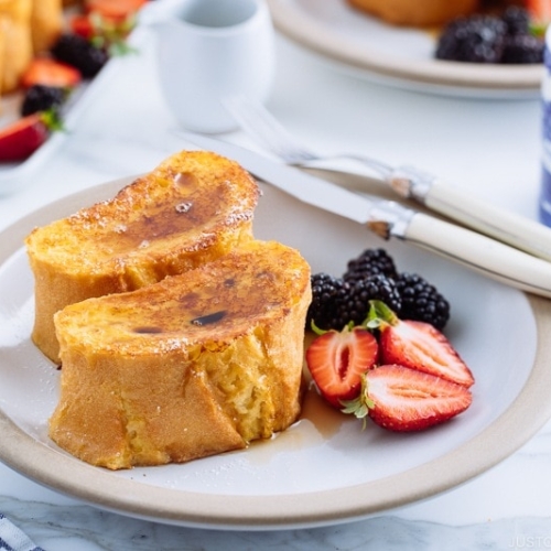 A plate containing French toast, strawberries, and black berries.