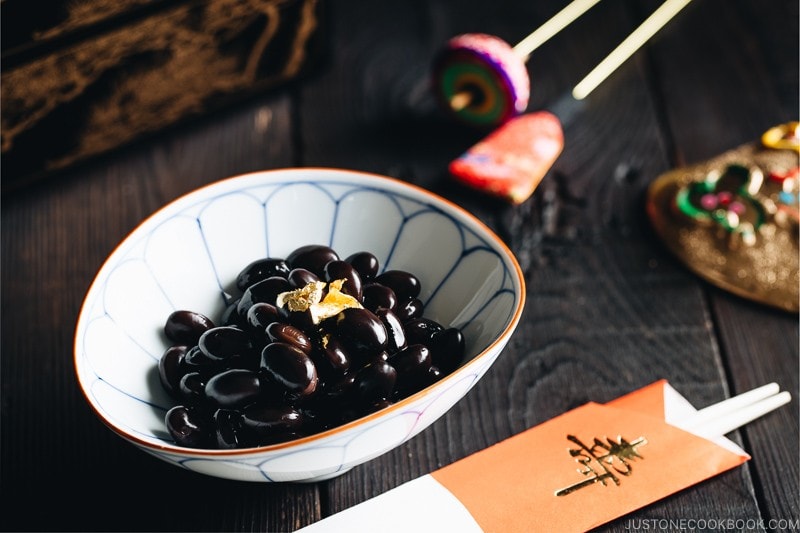 Sweet black soybeans garnished with a gold leaf in a Japanese blue and white bowl.