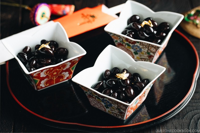 Sweet black soybeans garnished with gold leaf on Japanese red and gold dishes.