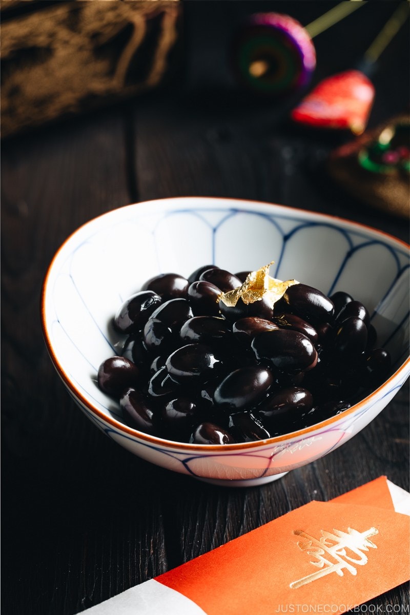 Sweet black soybeans garnished with a gold leaf in a Japanese blue and white bowl.