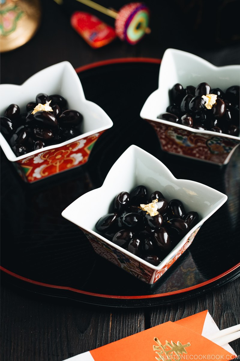 Sweet black soybeans garnished with a gold leaf in Japanese red and gold dishes.