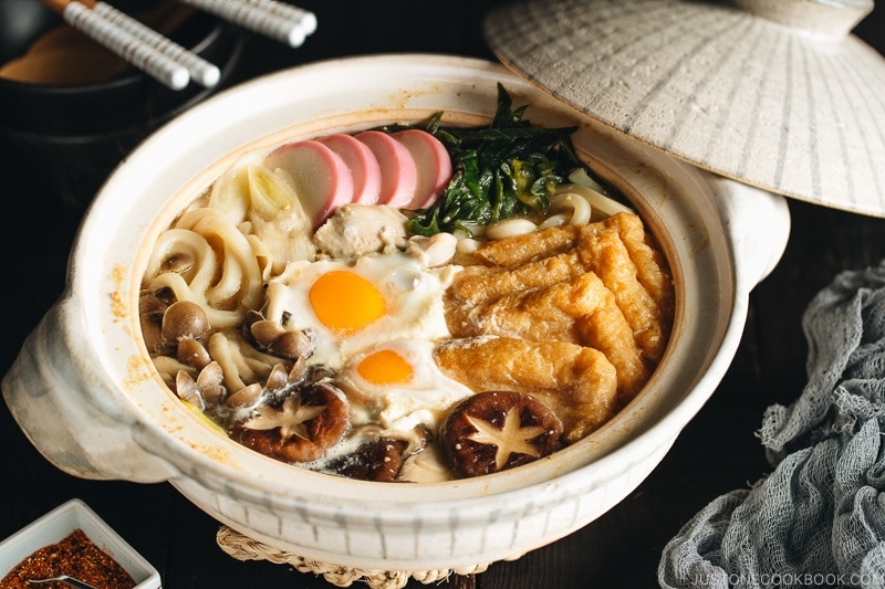 A donabe containing udon noodles, chicken, fish cakes, deep fried tofu, mushrooms, and leeks in a hearty miso broth.