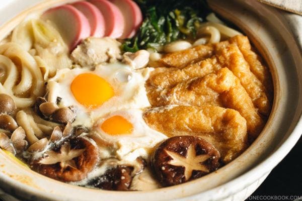 A donabe containing udon noodles, chicken, fish cakes, deep fried tofu, mushrooms, and leeks in a hearty miso broth.