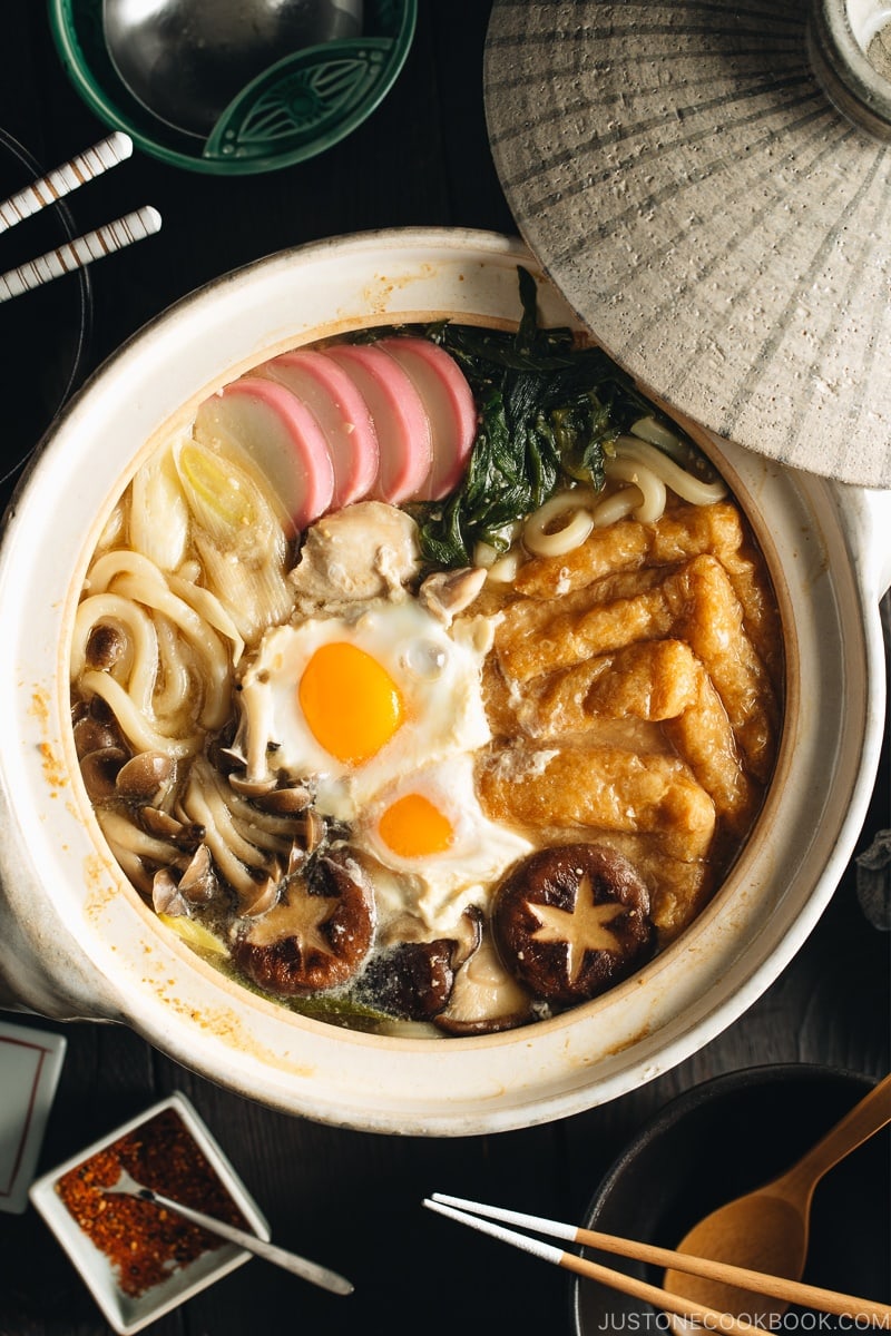 A donabe containing udon noodles, chicken, fish cakes, deep fried tofu, mushrooms, and leeks in a hearty miso broth.