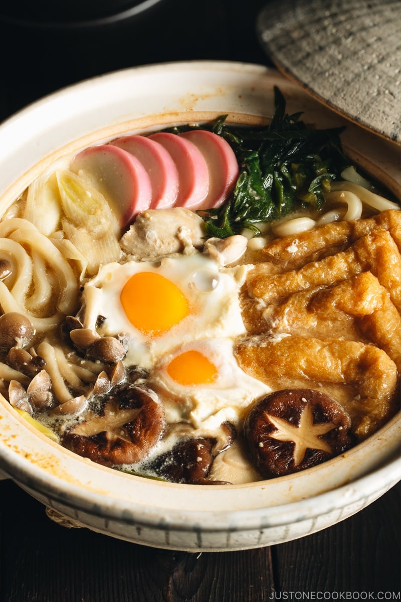 A donabe containing udon noodles, chicken, fish cakes, deep fried tofu, mushrooms, and leeks in a hearty miso broth.