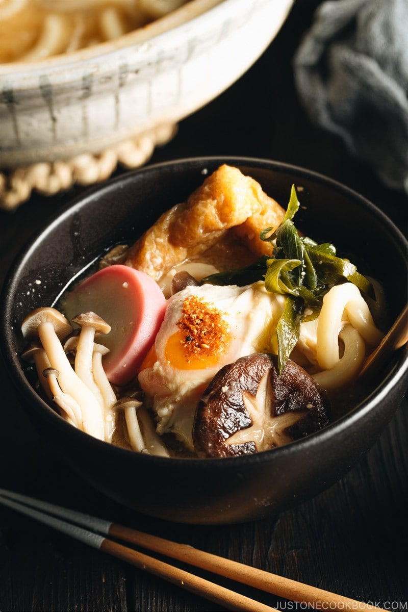 A donabe containing udon noodles, chicken, fish cakes, deep fried tofu, mushrooms, and leeks in a hearty miso broth.