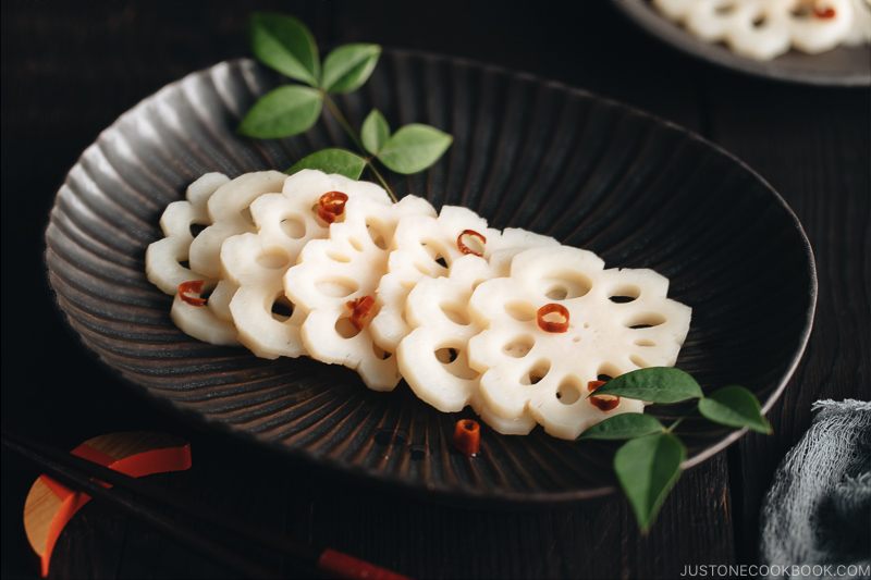 A black plate containing Pickled Lotus Root (Su Renkon), garnished with chopped red chili pepper.