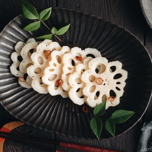 A black plate containing Pickled Lotus Root (Su Renkon), garnished with chopped red chili pepper.