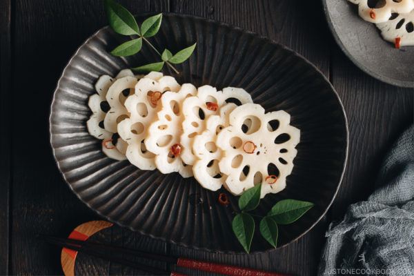 A black plate containing Pickled Lotus Root (Su Renkon), garnished with chopped red chili pepper.