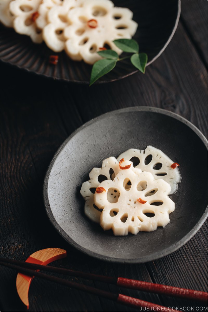 A black plate containing Pickled Lotus Root (Su Renkon), garnished with chopped red chili pepper.