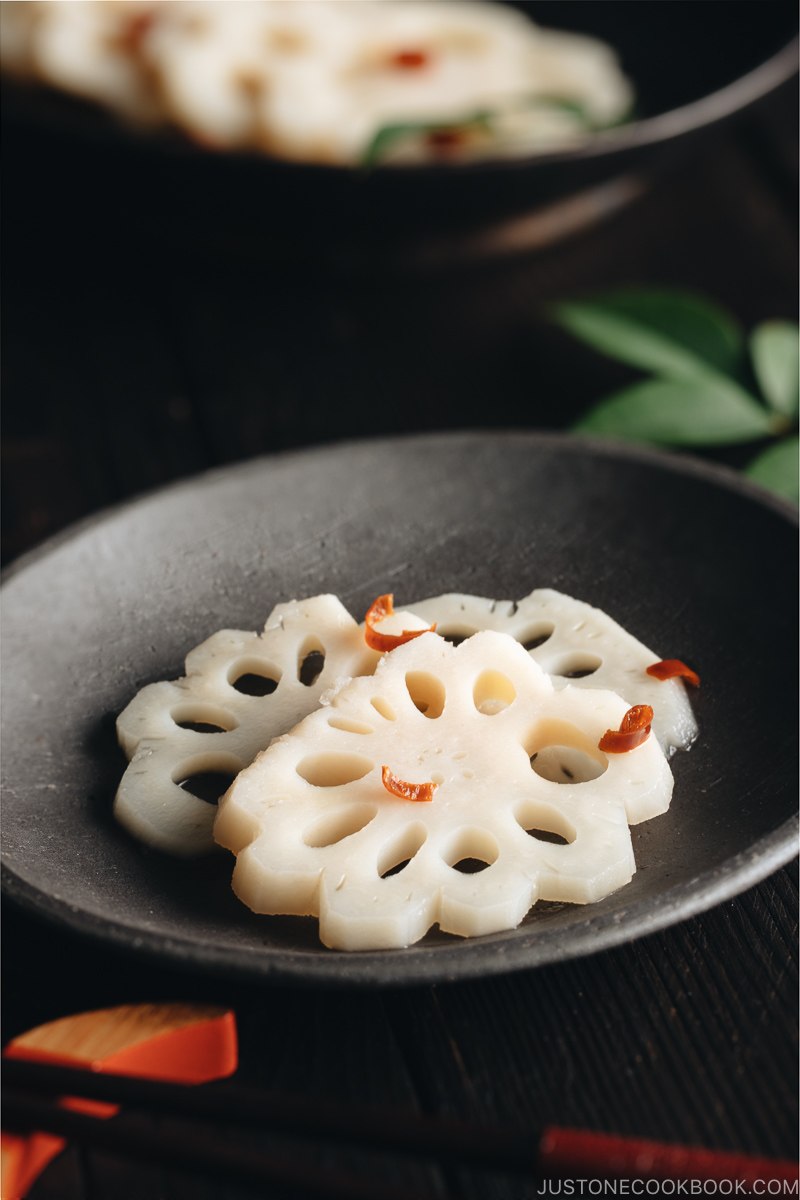 A black plate containing Pickled Lotus Root (Su Renkon), garnished with chopped red chili pepper.