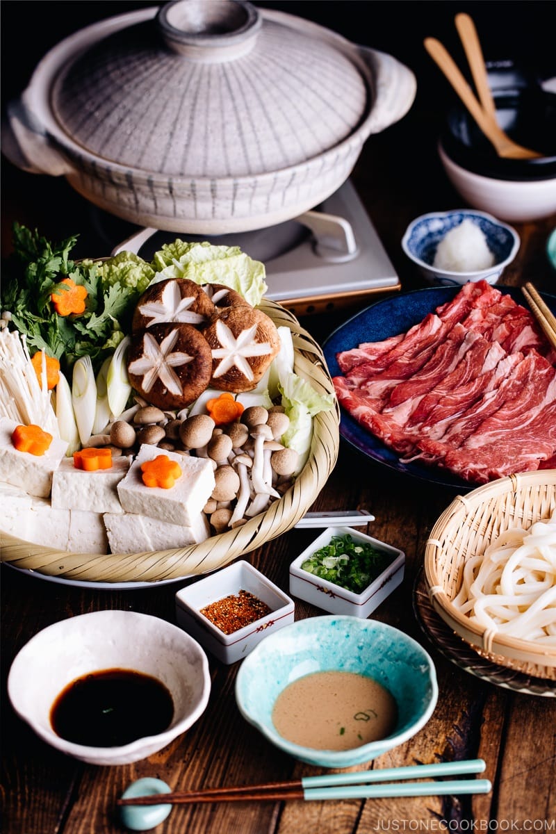 Tablesetup for shabu shabu - donabe hot pot, vegetables, meat, udon, and dipping sauces.