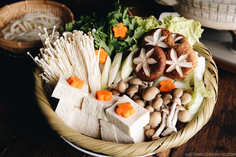 Assorted vegetables, tofu, and mushrooms in a bamboo basket, ready to cook in Shabu Shabu.