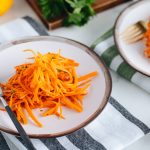 Carrot salad on a white plate with gray rim.