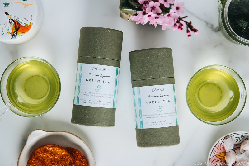 Two types of Japanese green tea in a cup and their containers along with tea pot.