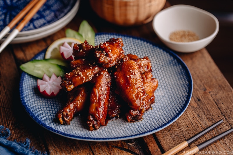 Orange teriyaki chicken wings on a blue patter.