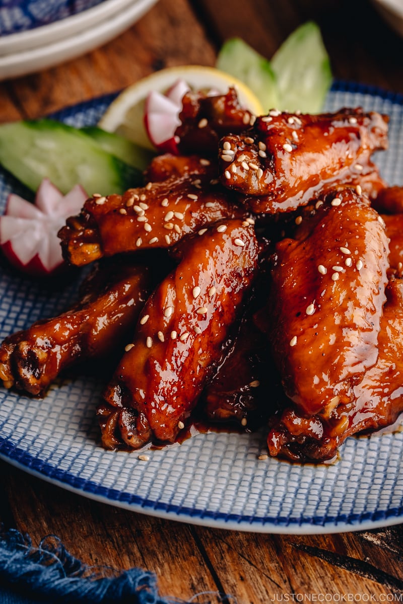 Orange teriyaki chicken wings on a blue patter.