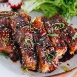 Sticky Asian Ribs on a white platter, topped with sprinkle of green onion.