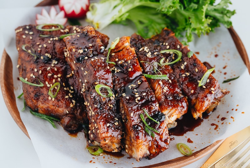 Sticky Asian Ribs on a white platter, topped with sprinkle of green onion.