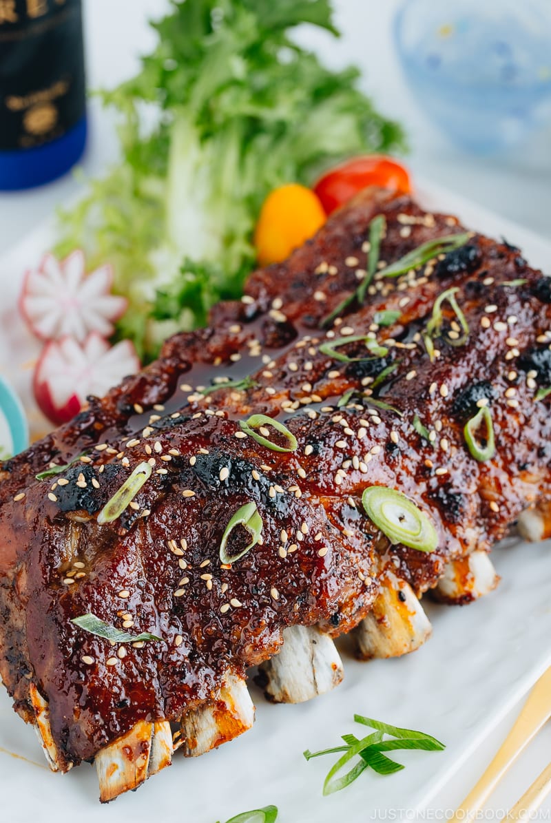 Sticky Asian Ribs on a white platter, topped with sprinkle of green onion.