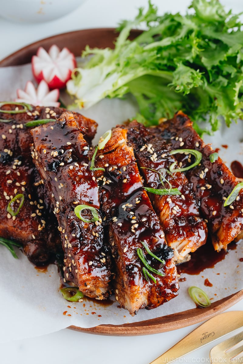 Sticky Asian Ribs on a white platter, topped with sprinkle of green onion.