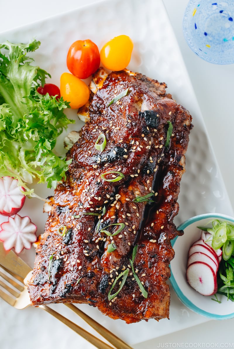 Sticky Asian Ribs on a white platter, topped with sprinkle of green onion.