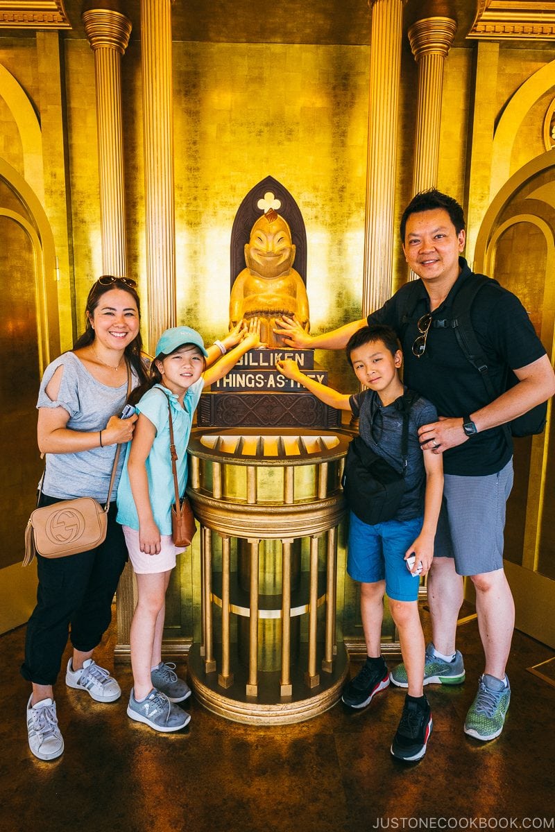 a family rubbing the feet of enshrined Billiken at Tsutenkaku Tower - Osaka Guide: Tsutenkaku and Shinsekai District | www.justonecookbook.com