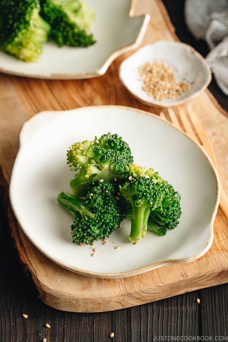 A white plate containing blanched broccoli tossed with sesame seeds.
