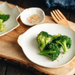 A white plate containing blanched broccoli tossed with sesame seeds.