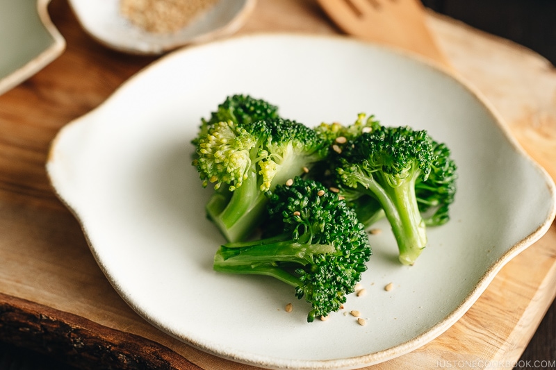 A white plate containing blanched broccoli tossed with sesame seeds.