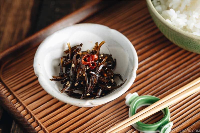 Simmered kombu in a small dish next to a bowl of steamed rice.