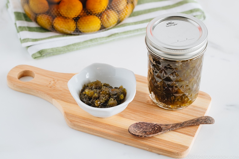 Plum jam in a white small bowl. Plum jam in a jar and plum wine in the back.