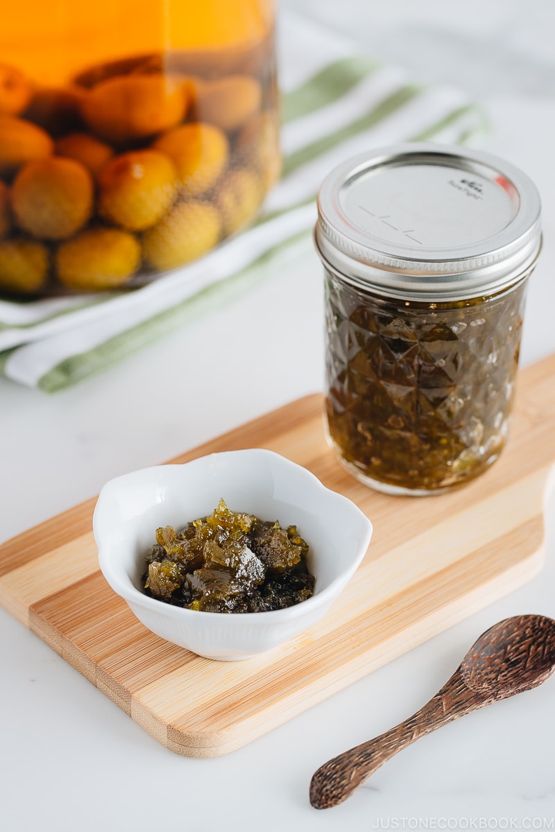 Plum jam in a white small bowl. Plum jam in a jar and plum wine in the back.