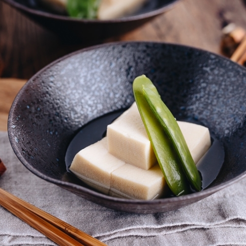 Simmered koyadofu with snow peas in a black ceramic bowl.