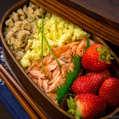 Ground chicken, egg, and salmon over rice in a wooden bento box.
