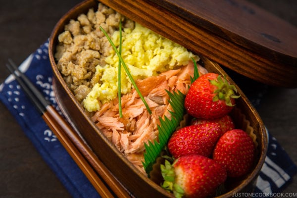 Ground chicken, egg, and salmon over rice in a wooden bento box.
