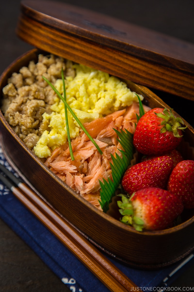 Ground chicken, egg, and salmon over rice in a wooden bento box.