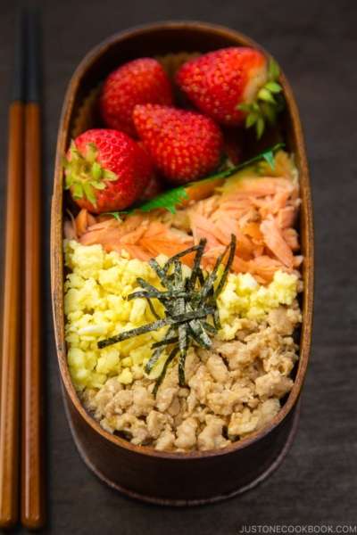 Ground chicken, egg, and salmon over rice in a wooden bento box.