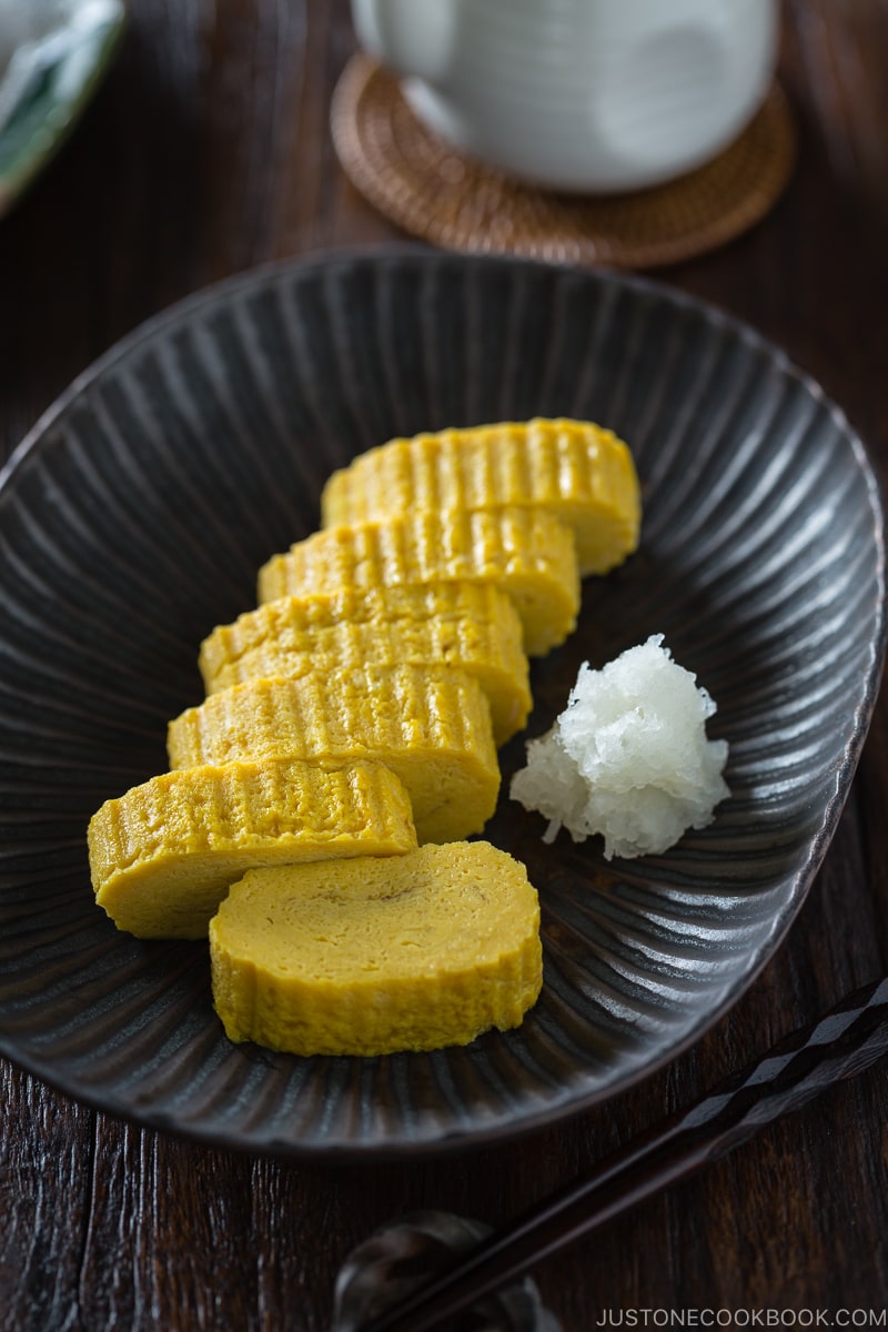 Tamagoyaki and grated daikon on a black plate.