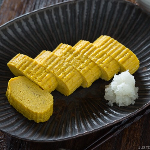 Tamagoyaki and grated daikon on a black plate.